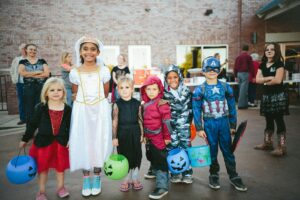 Group of children standing in a line all wearing various costumes and smiling.